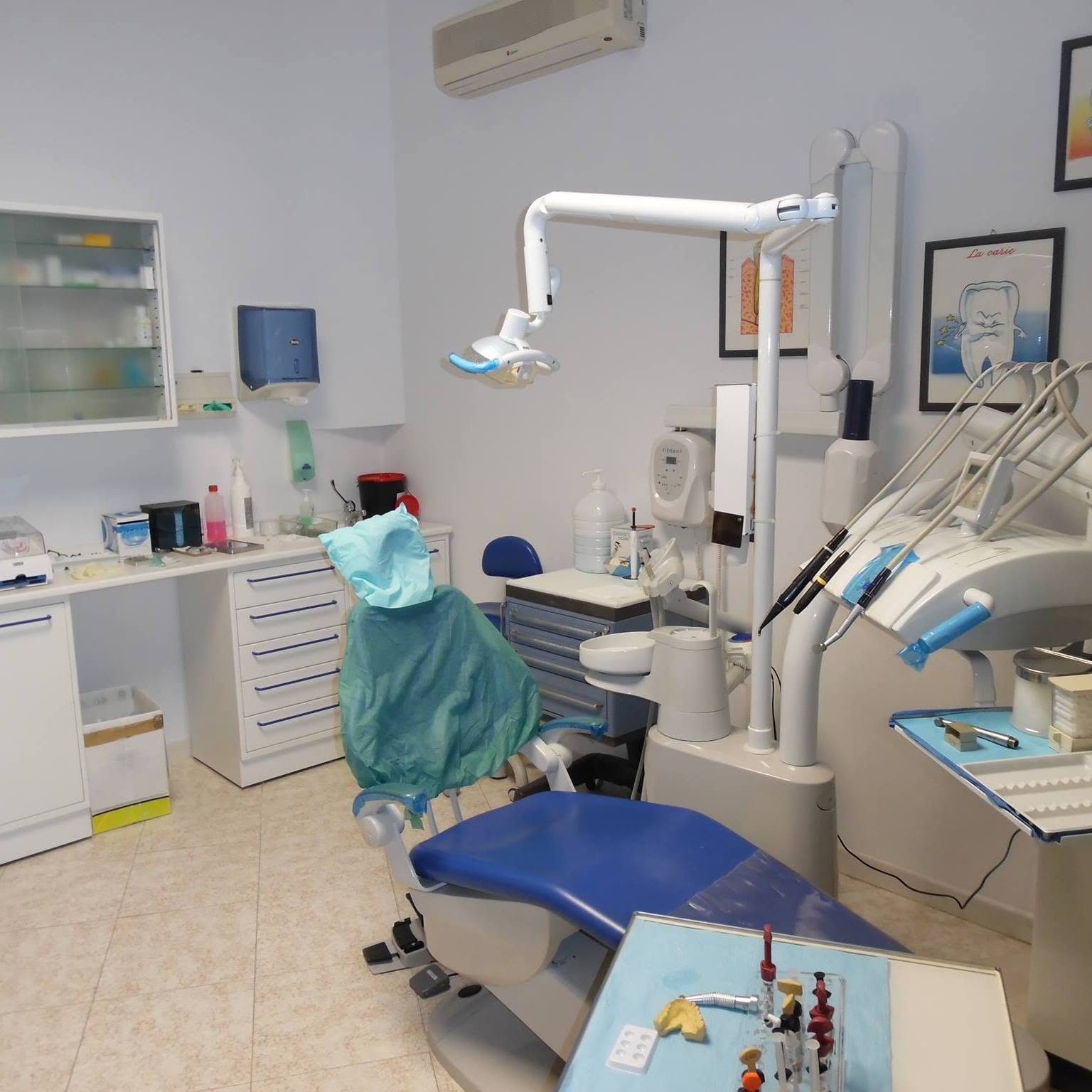 Dental treatment room with a blue chair, overhead lamp, cabinetry and dental equipment, shown in a well-lit interior view.