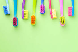 Several brightly colored toothbrushes are arranged vertically against a bright green background, with soft even lighting and ample empty space.