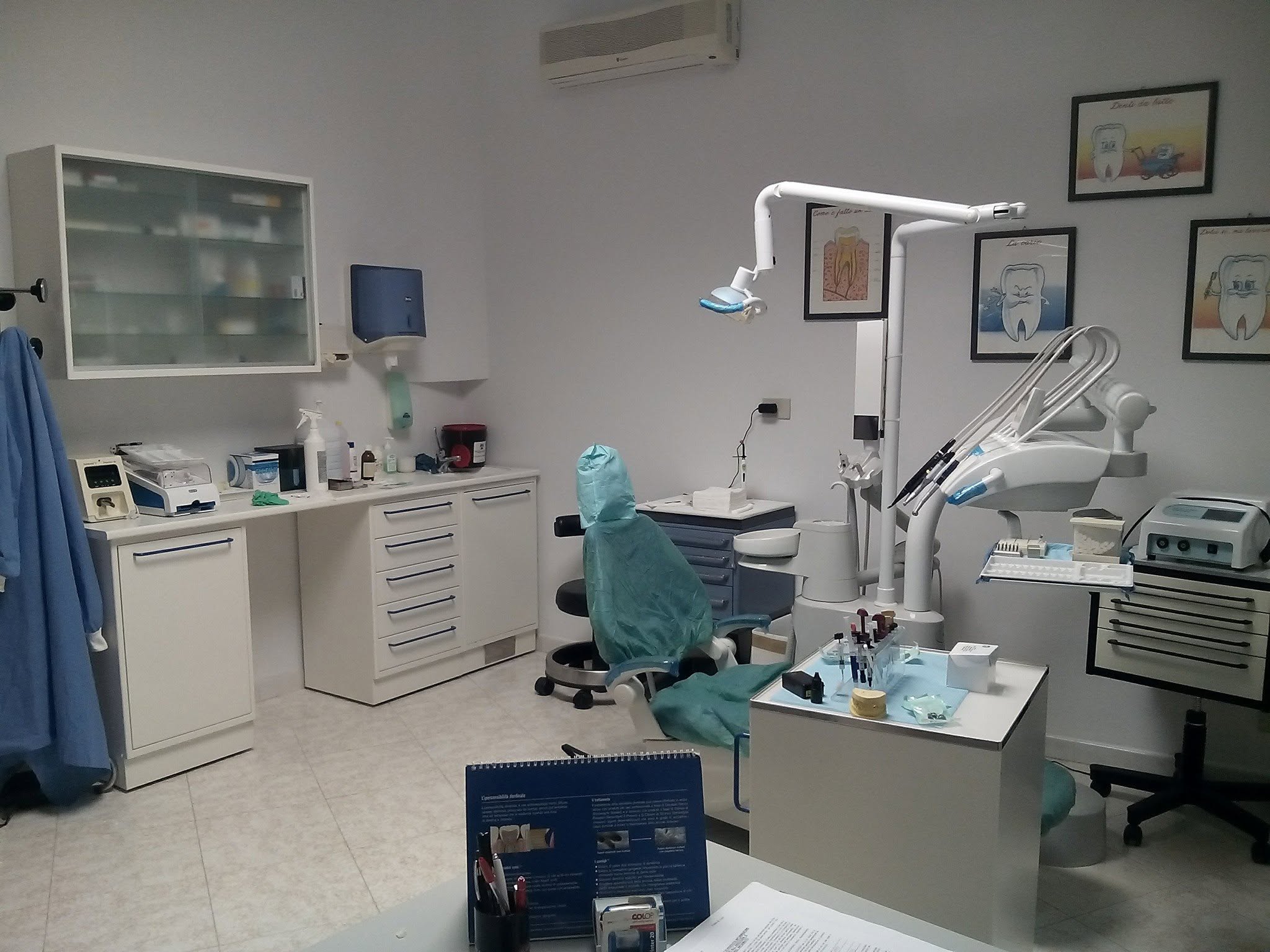 Bright dental treatment room with a dental chair, overhead lamp, cabinetry, instruments and clinical equipment in a wide interior view.